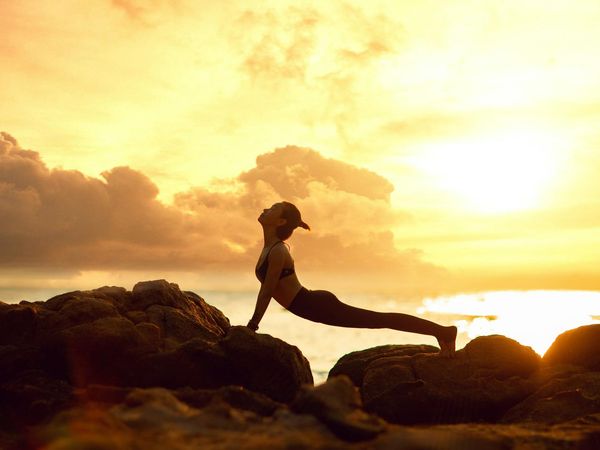 Silhouette of a person in a yoga warrior pose against a sunset.